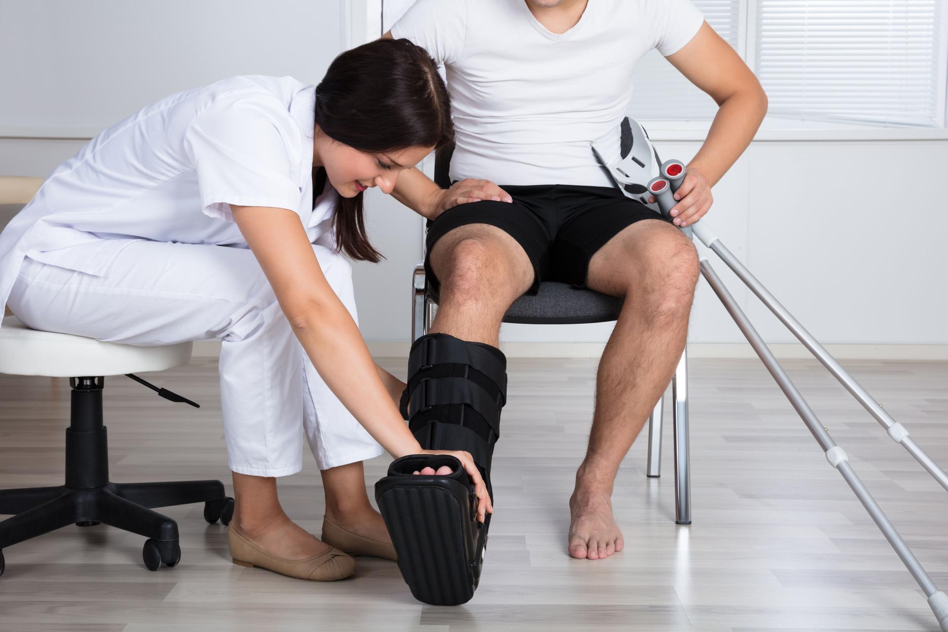 Female Doctor Putting Walking Brace On Person's Leg